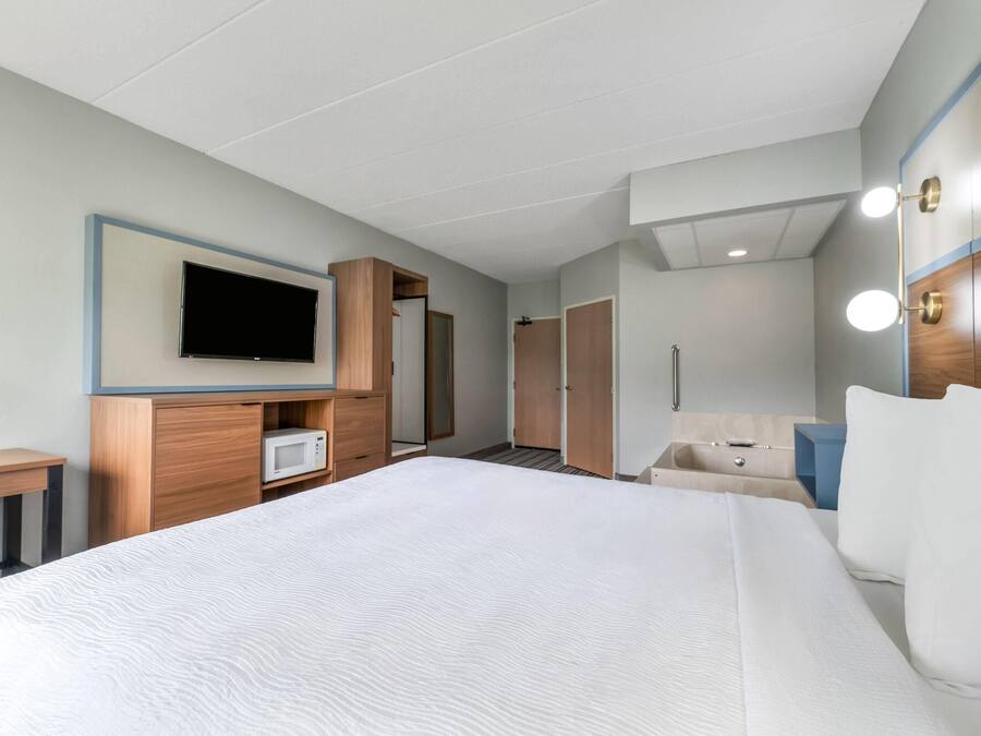 Quarto de hotel com uma cama grande, televisão na parede, guarda-roupa, mesa de cabeceira e espelho com iluminação.