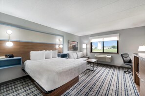Une chambre d’hôtel avec un grand lit, des tables de chevet, un bureau, une chaise, un canapé, une fenêtre avec vue et un luminaire au plafond.
