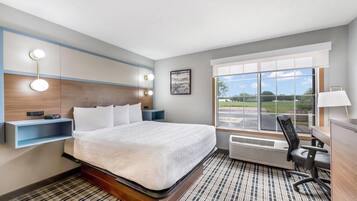A hotel room with a large bed, bedside tables, a desk with a chair, a window with a view, and a wall-mounted light fixture.