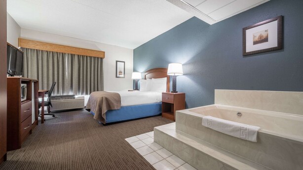 Habitació d'hotel amb llit, taulells laterals, televisió, escriptori, cadira, làmpada d'escriptori, finestra amb cortines, quadre a la paret i banyera.