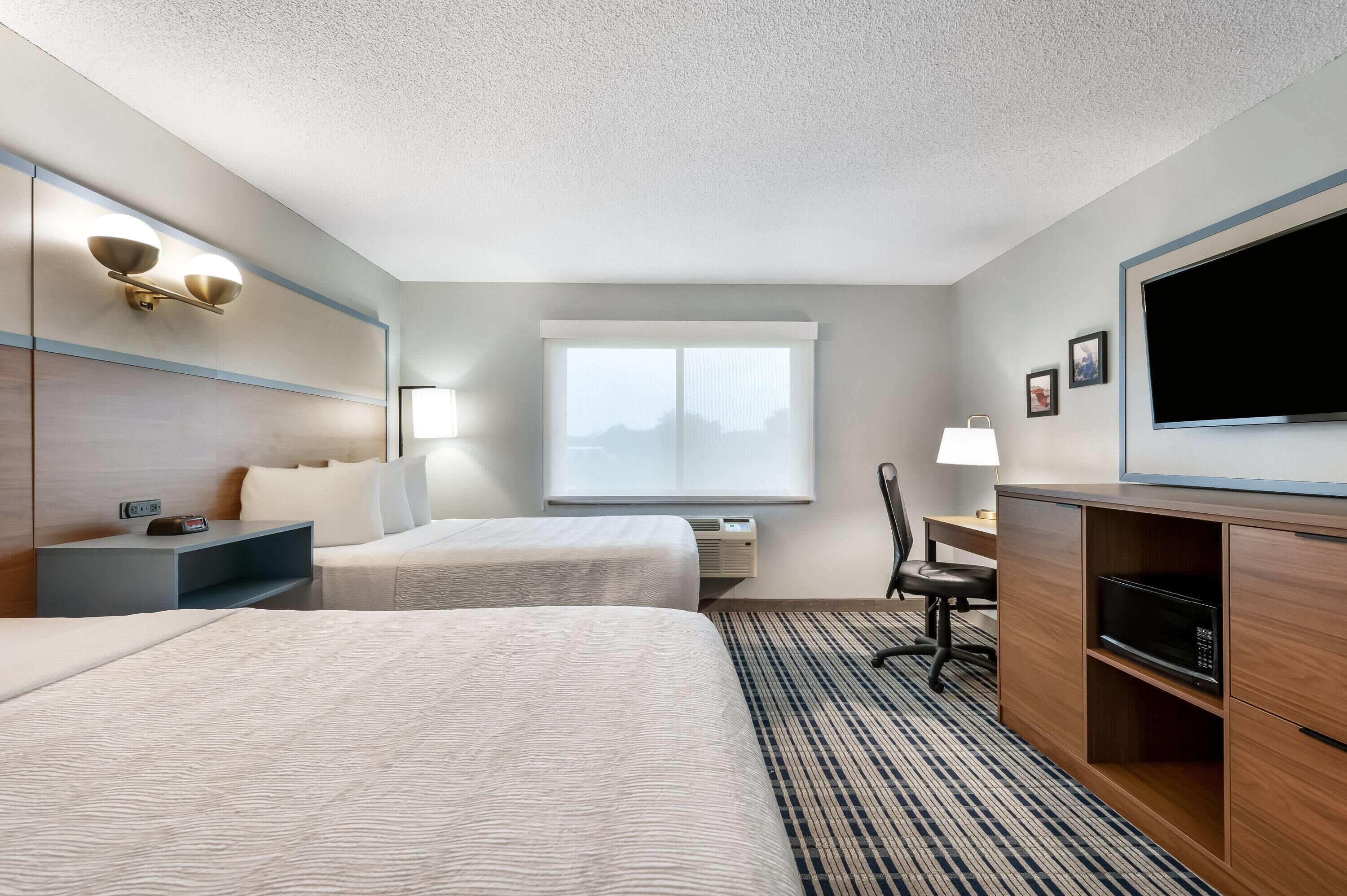 A hotel room with two beds, a desk, a chair, a television, and a window with a view.
