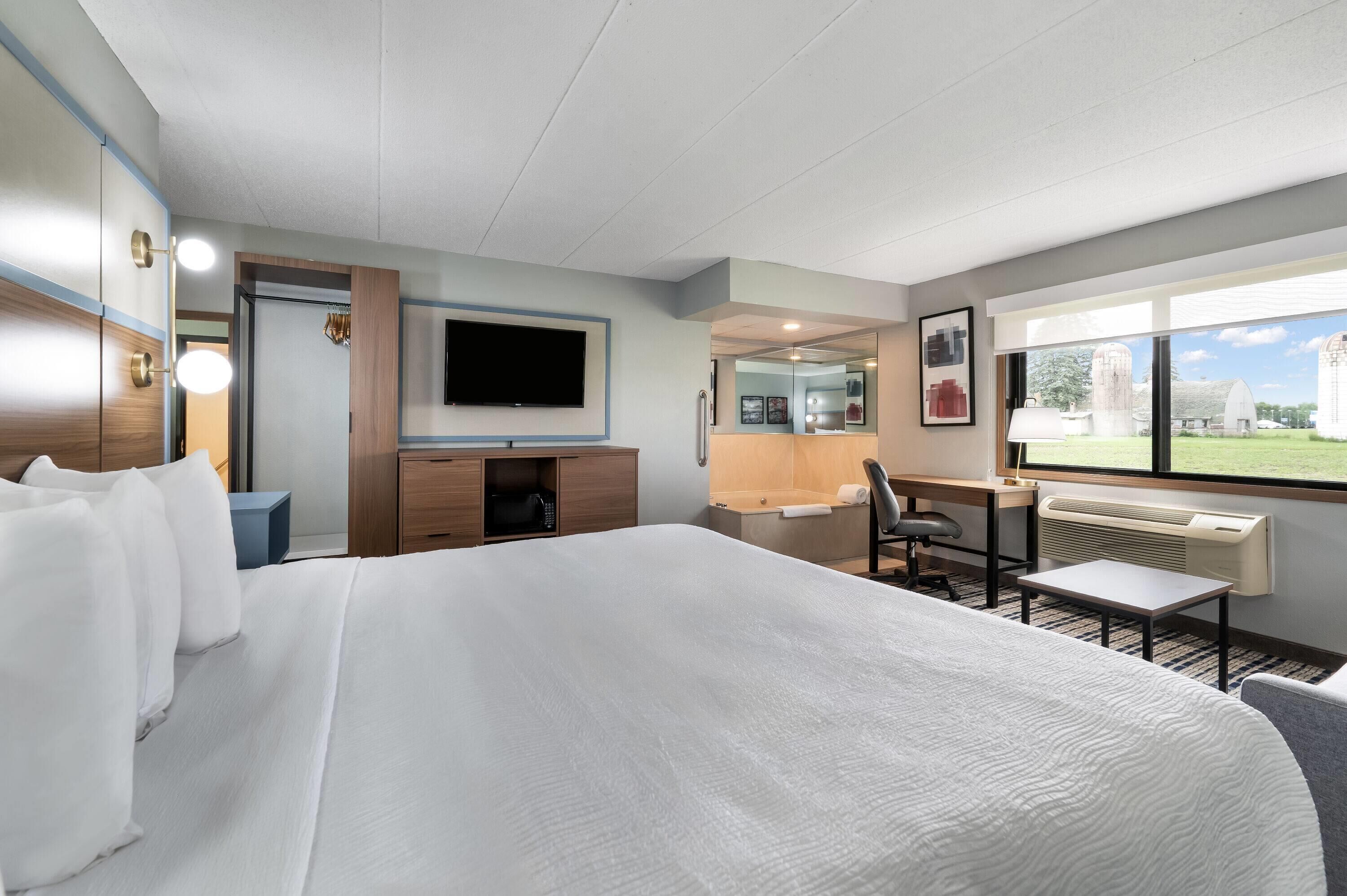 A hotel room with a large bed, a desk, a chair, a television, and a window with a view of the countryside.