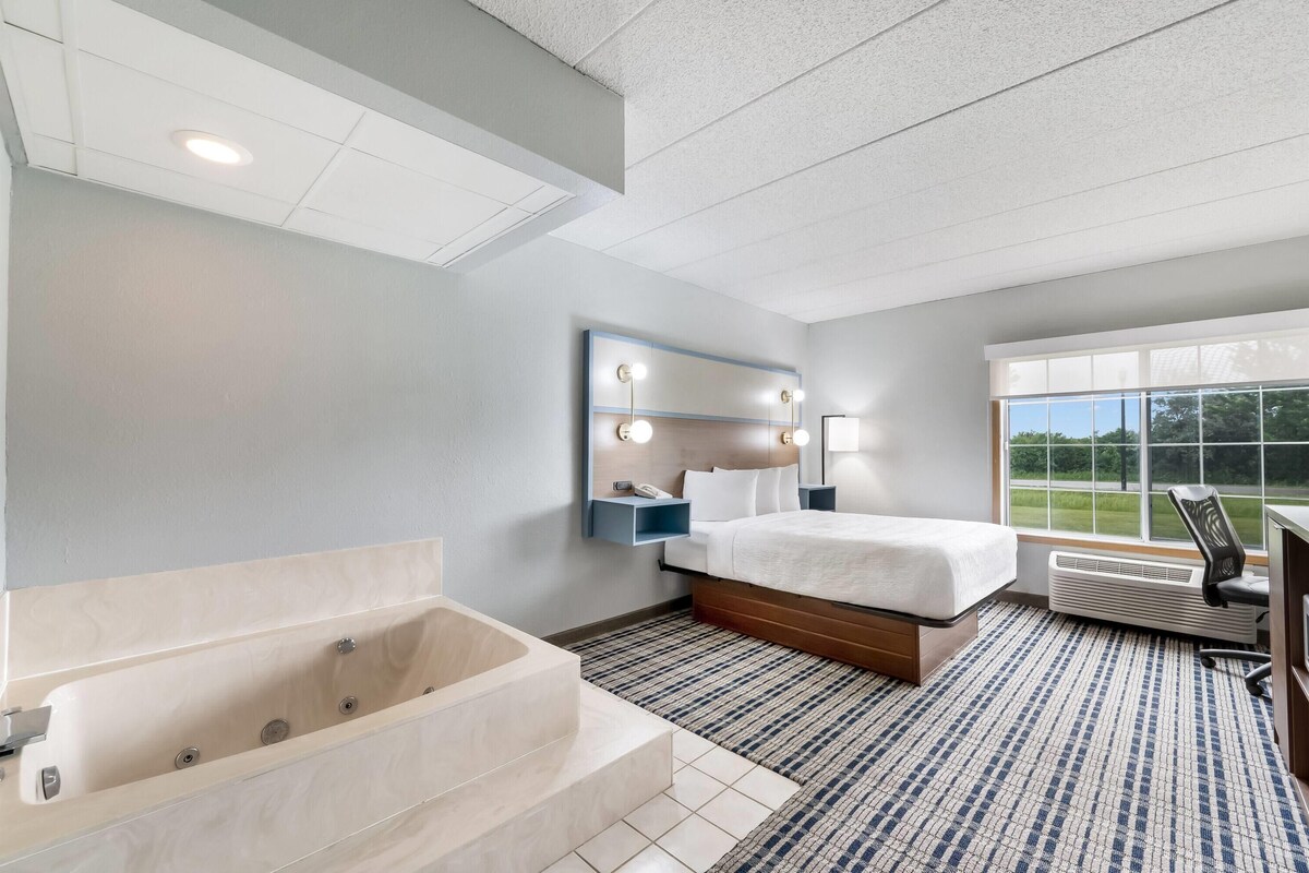Una habitación de hotel moderna con una cama grande, una bañera empotrada y un ventanal con vistas al exterior.
