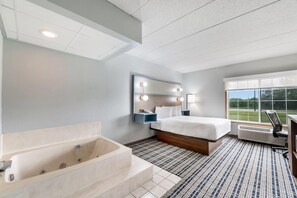Ein modernes Hotelzimmer mit einem großen Bett, einer integrierten Badewanne und einem großen Fenster mit Blick ins Freie.