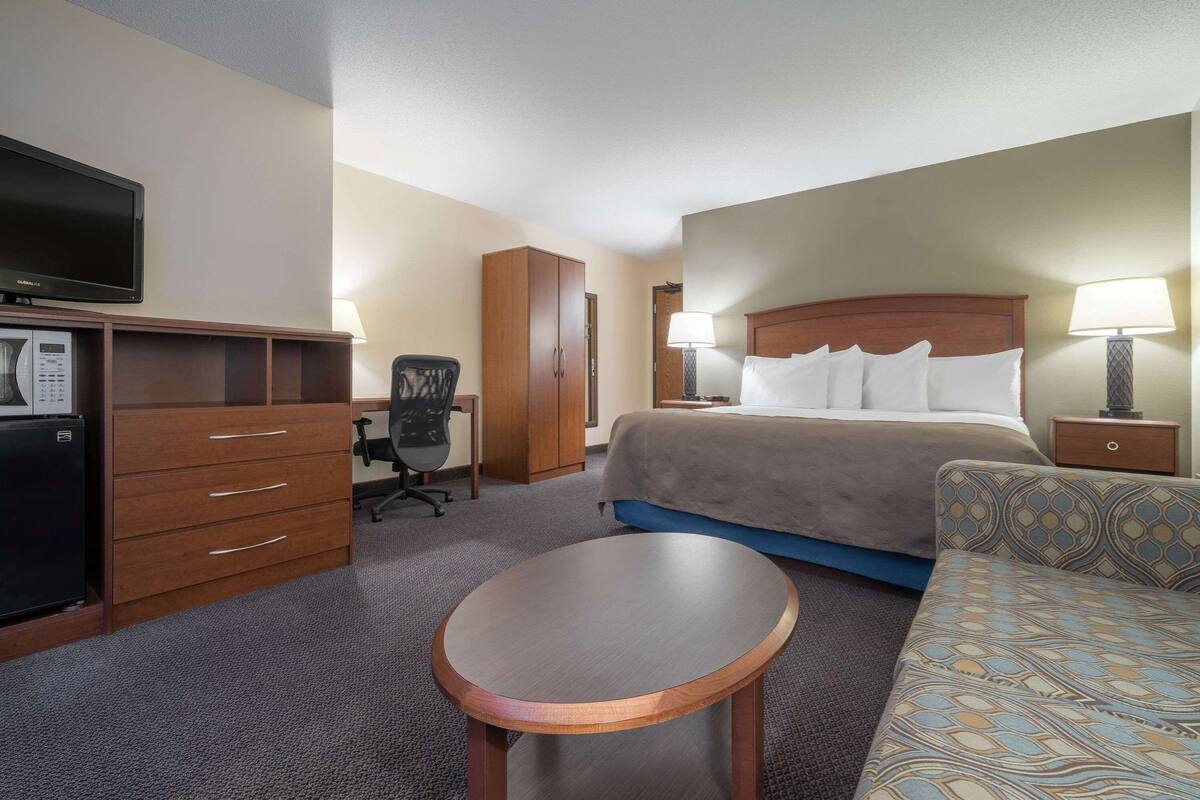Habitación de hotel con cama, escritorio, computadora, silla, televisión y una mesita.