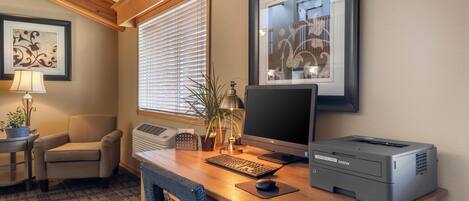 A home office with a desk, computer, printer, chair, lamp, and framed artwork.