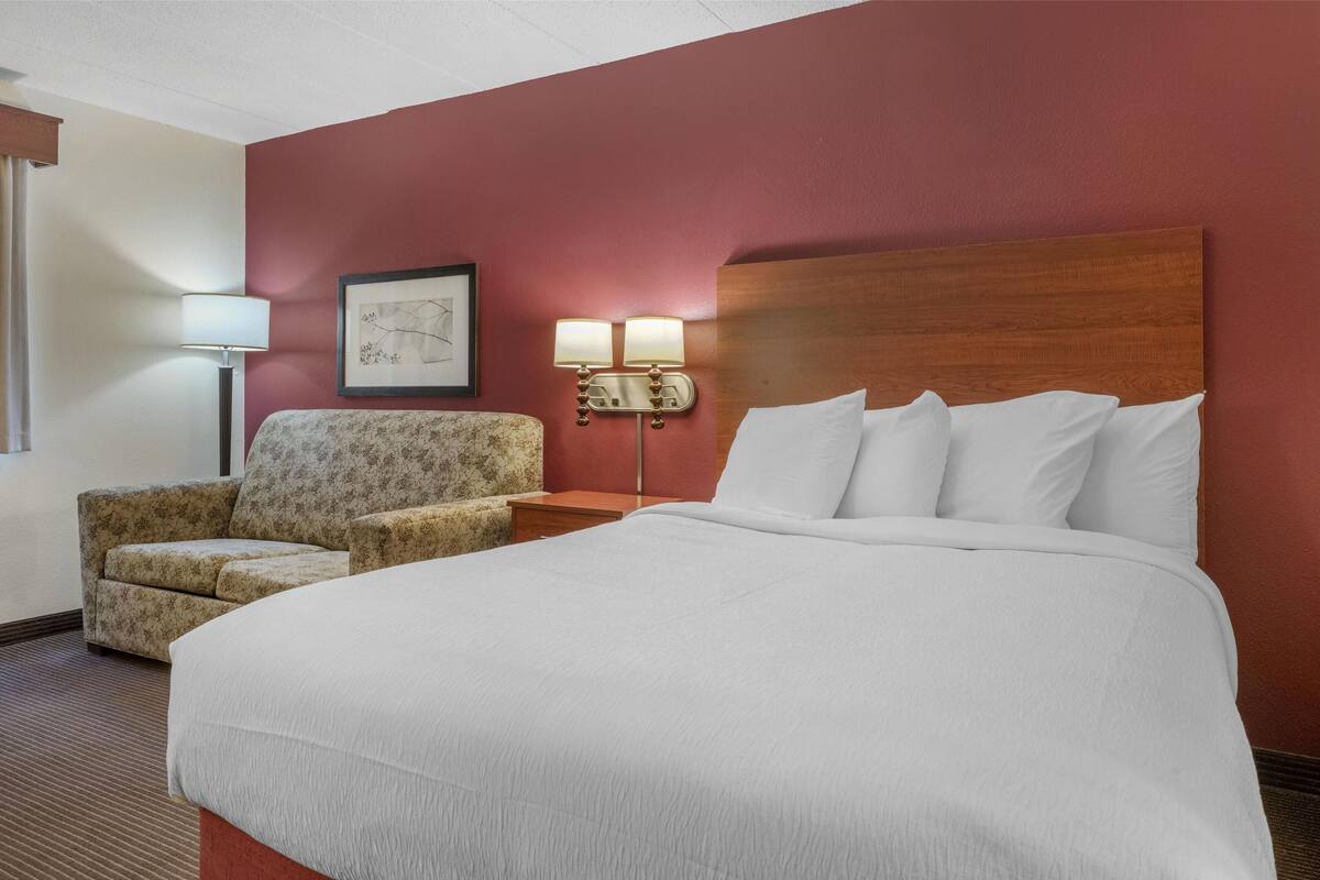 A hotel room with a large bed, a chair, a nightstand, and a wall-mounted lamp.