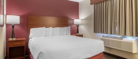Une chambre d’hôtel avec un grand lit, deux tables de chevet, un climatiseur fixé au mur et une fenêtre avec des rideaux.