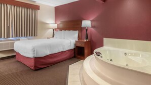 A hotel room with a bed, bedside table, lamp, and a large bathtub.