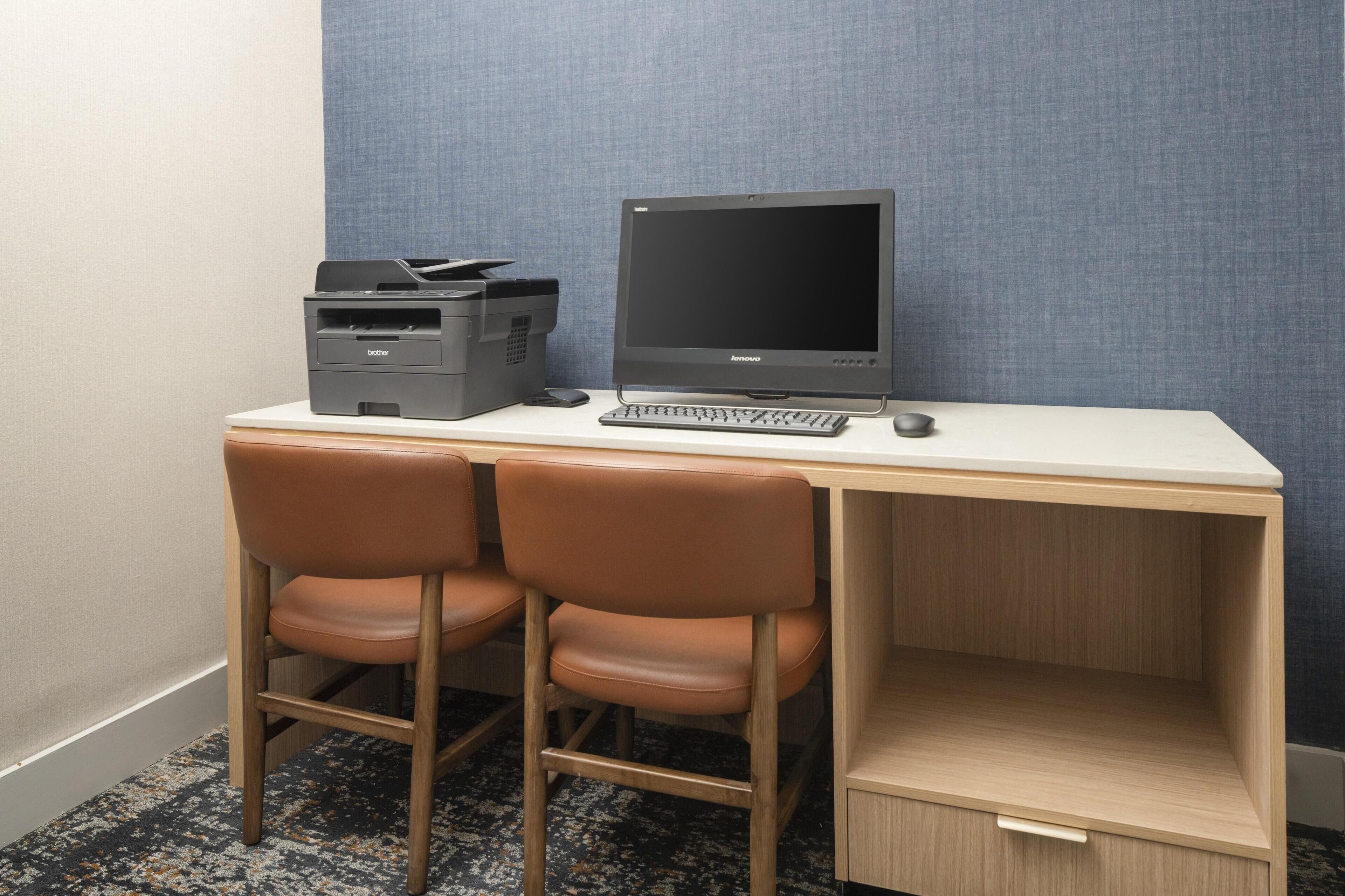 Un petit bureau comprenant un bureau, deux chaises, un écran d’ordinateur, un clavier, une souris et une imprimante.