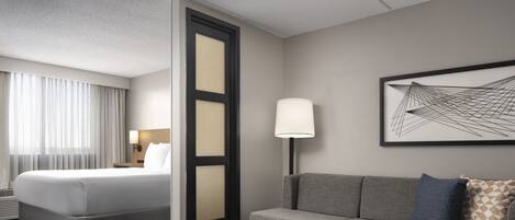 A hotel room with a bed, a sofa, a small table, a lamp, and a framed abstract artwork on the wall.