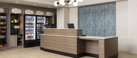 A reception area with a wooden reception desk, a checkout counter, and refrigerated beverage dispensers labeled 'CHECKOUT,' 'RESTORE,' and 'REFRESH.'