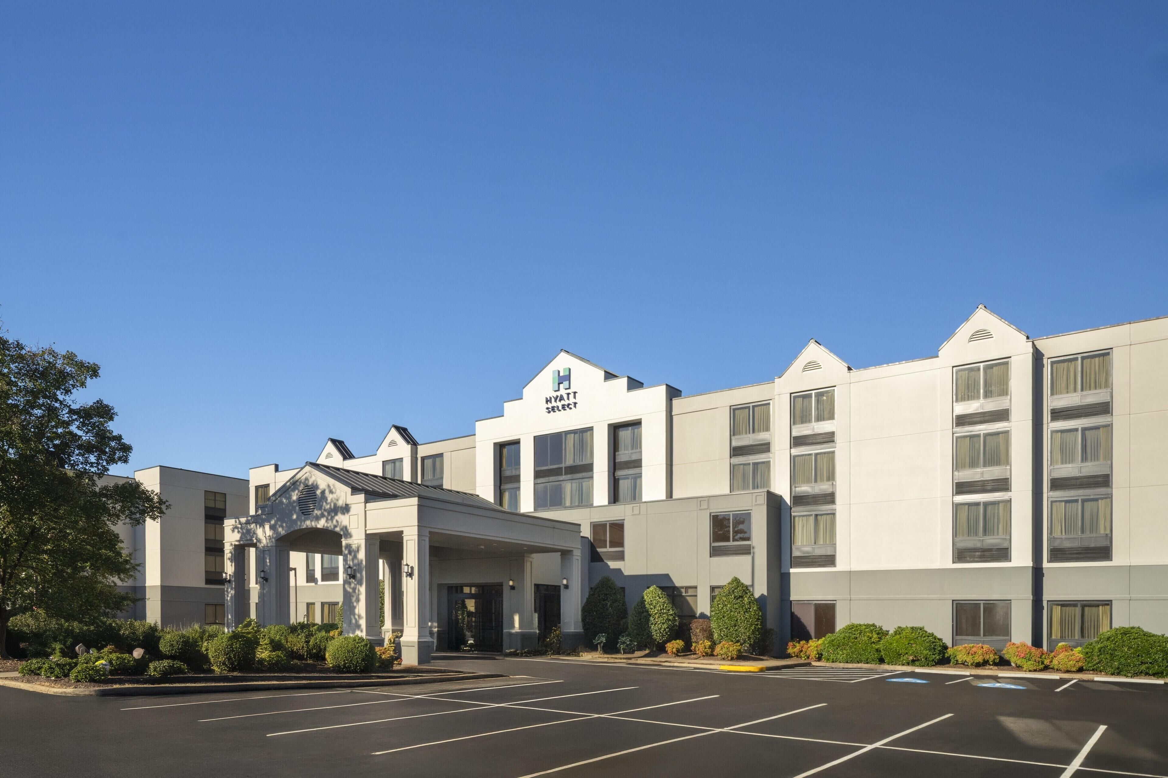 A multi-story hotel with a central entrance, a parking lot, and a clear blue sky.