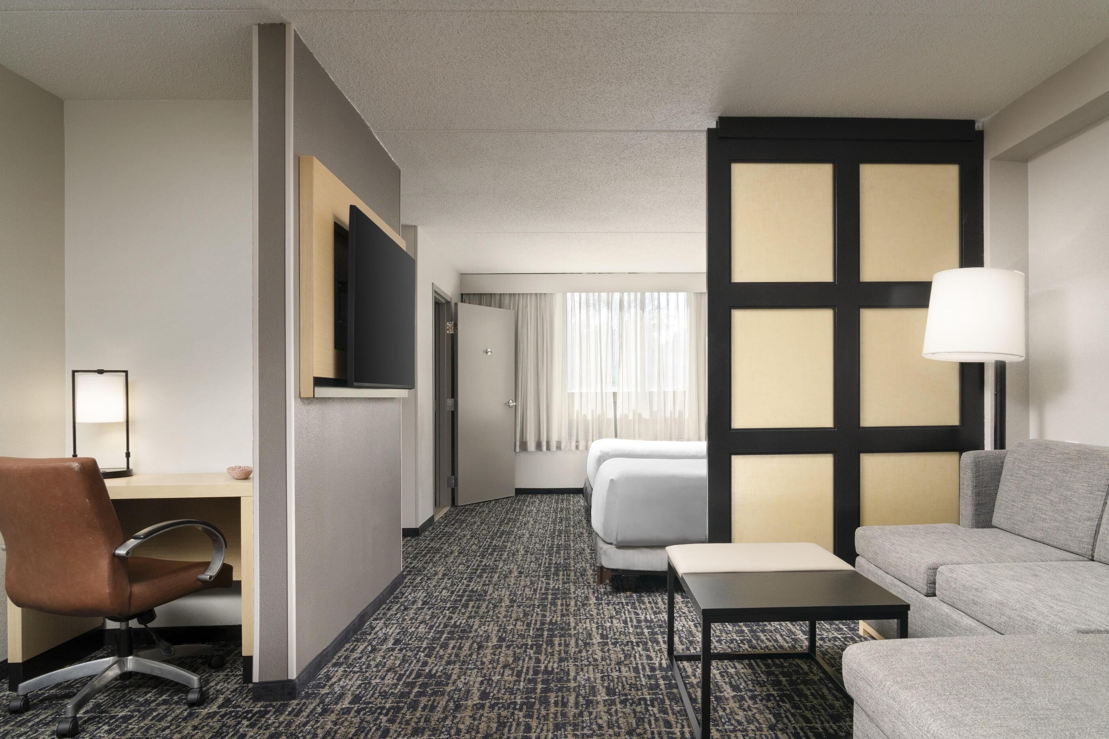 A hotel room with a bed, a sofa, a desk with a chair, a lamp, and a TV.