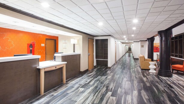 Un vestíbulo de hotel con un largo pasillo, mostrador de recepción y zona de estar.