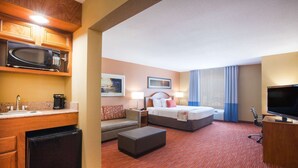 Habitación de hotel con kitchenette, cama, sofá, televisor y ventana con cortinas.