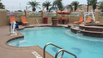 A swimming pool with a diving board, lounge chairs, and a small hot tub area.