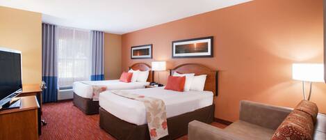 Quarto de hotel com duas camas, uma escrivaninha, uma televisão e um sofá.