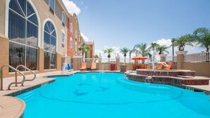 Una piscina con solárium de baldosas, sillas de descanso y sombrillas.