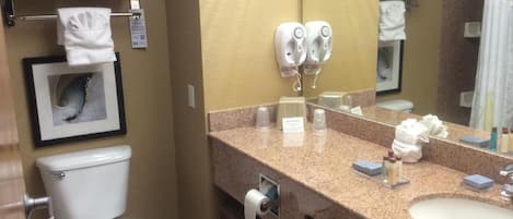 Un baño con inodoro, lavamanos, toallero, secamanos y un cuadro en la pared.