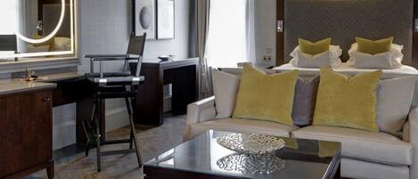 A modern hotel room with a sofa, a glass coffee table, a desk, and a large mirror.