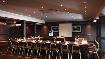A conference room with a long table, multiple chairs, nameplates, and a projector screen.
