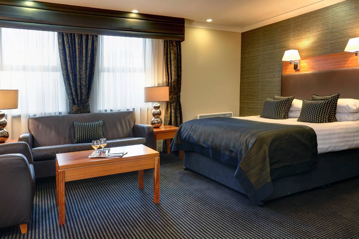 A hotel room with a bed, a sofa, a coffee table, and two lamps.