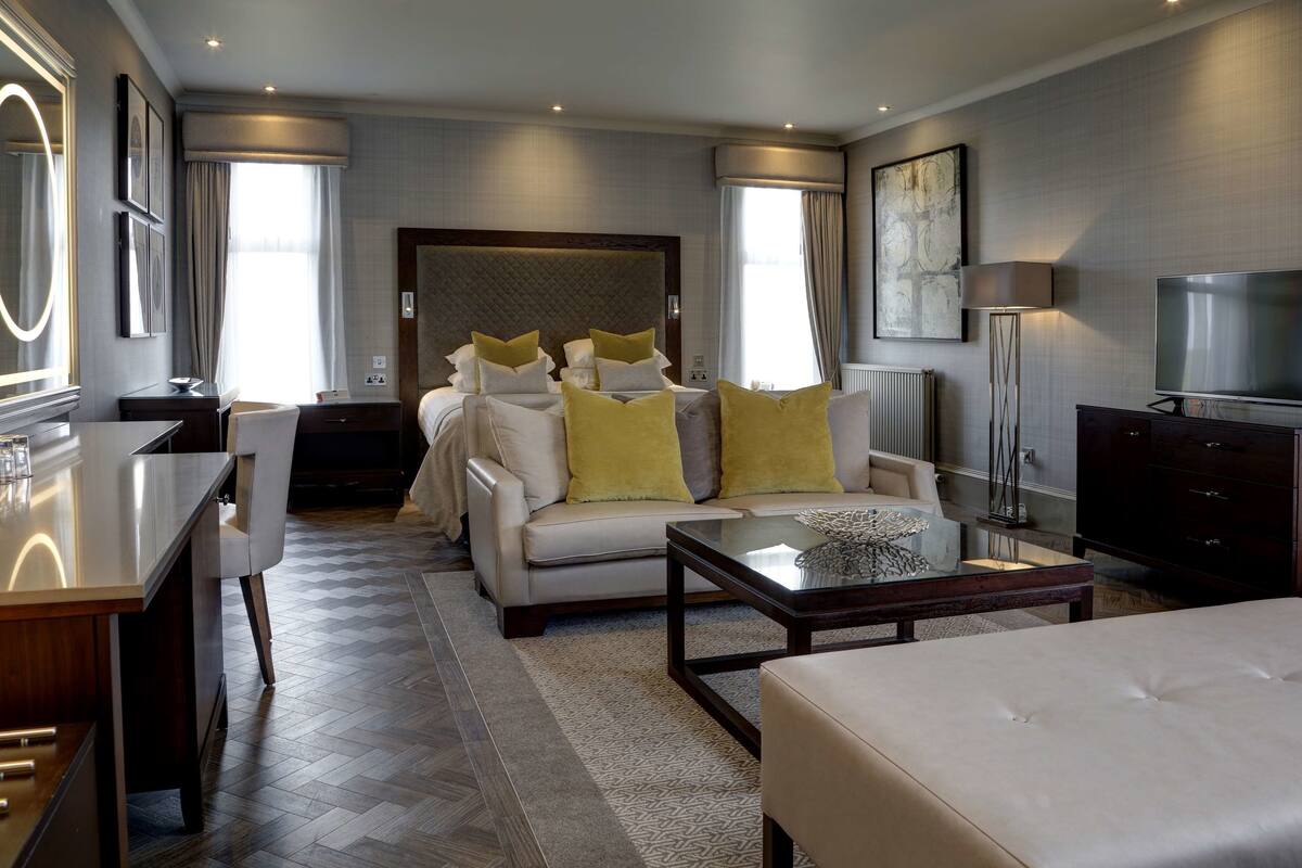 A modern hotel room with a large bed, a sofa, a coffee table, a TV, and a desk.