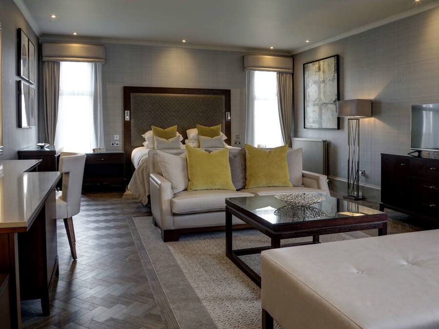 A modern hotel room with a large bed, a sofa, a coffee table, a TV, and a desk.