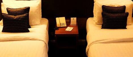 A hotel room with two beds, each with a pillow and a lamp on a bedside table.