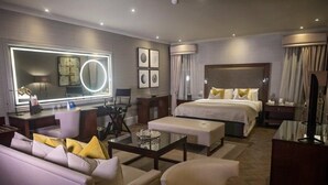 A modern hotel room with a large bed, a sitting area with a sofa and armchairs, a desk with a chair, a large mirror, and a television. - Best Western Garfield House Hotel (Glasgow)