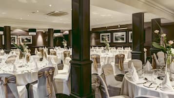 Un salón de banquetes con mesas redondas dispuestas para un evento formal, con manteles blancos, fajas doradas y centros de mesa florales.