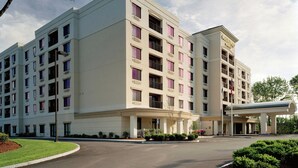 A multi-story hotel with a central entrance, a covered parking area, and a landscaped front yard.