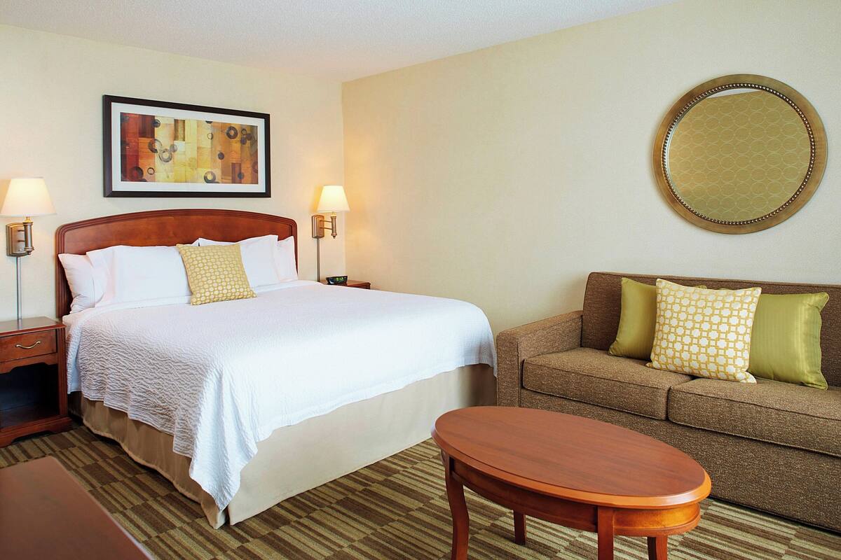 A hotel room with a bed, a sofa, a round mirror, and two bedside lamps.