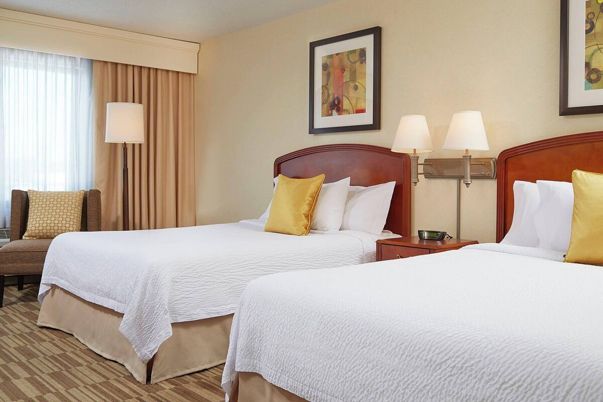 A hotel room with two beds, a sofa, a lamp, and a painting on the wall.