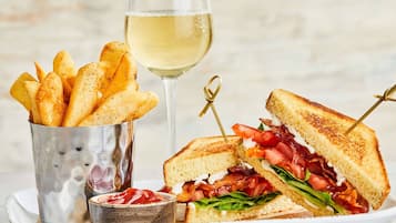 Sanduíche com bacon, alface e tomate, acompanhado de batatas fritas e um copo de vinho branco.