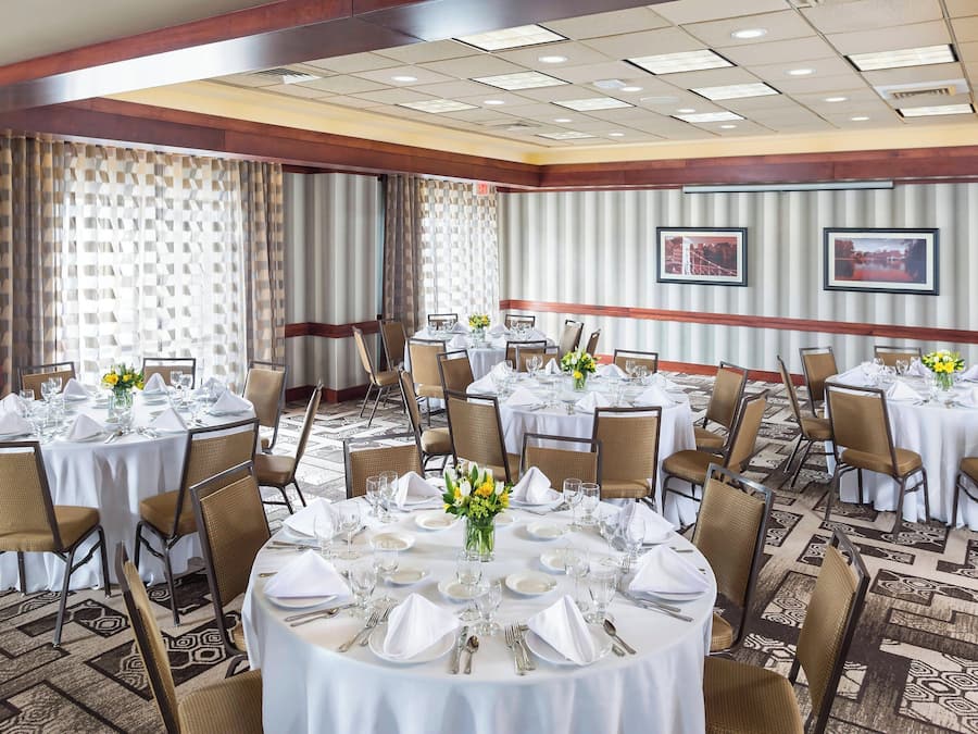 Un salón de banquetes con mesas redondas dispuestas para cenar, con manteles blancos, sillas y centros de mesa florales.