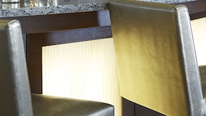 A bar area with a glass shelf displaying various bottles, a granite countertop, and two upholstered chairs.
