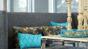 Una sala de estar moderna con un sofá gris, cojines estampados en color verde azulado y una mesa de centro de vidrio transparente con una bandeja decorativa azul.