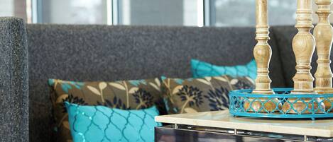 Ein modernes Wohnzimmer mit einem grauen Sofa, Kissen mit blaugrünem Muster und einem glasigen Couchtisch mit einer blauen Dekotasse.
