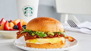 A breakfast sandwich on a plate with a cup and a fork in the background.