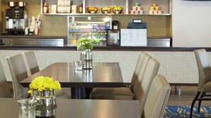 A hotel dining area with a long table, chairs, a vase with yellow flowers, and a coffee machine in the background.