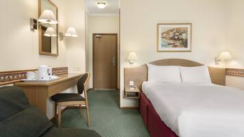Ett hotellrum med en säng, ett skrivbord, en stol och en tavla på väggen.