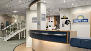 A reception desk with a digital screen, a sign for Days Inn, and a staircase in the background. - Days Inn by Wyndham Donington A50 (Derby)