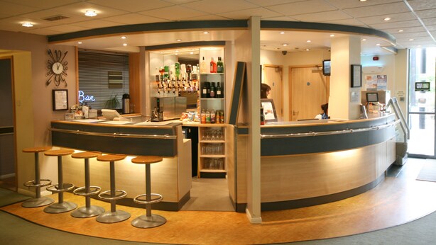 A bar area with stools, a counter, and shelves stocked with bottles. - Days Inn by Wyndham Donington A50 (Derby)