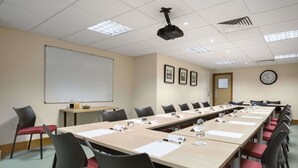 A conference room with a long table, chairs, a projector, a whiteboard, and a clock on the wall. - Days Inn by Wyndham Donington A50 (Derby)