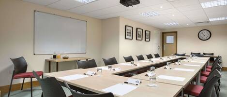 A conference room with a long table, chairs, a projector, a whiteboard, and a clock on the wall.