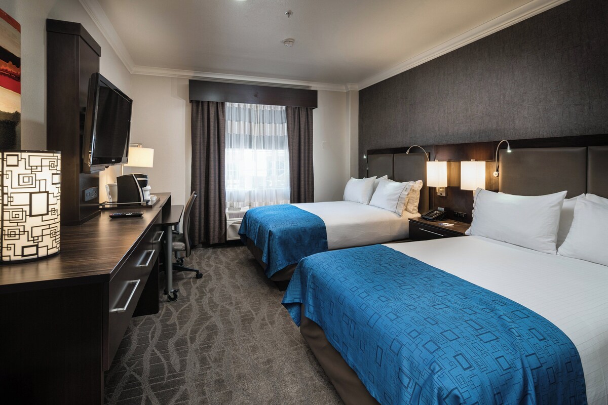 A hotel room with two beds, a desk with a TV, a lamp, and a nightstand with a phone.