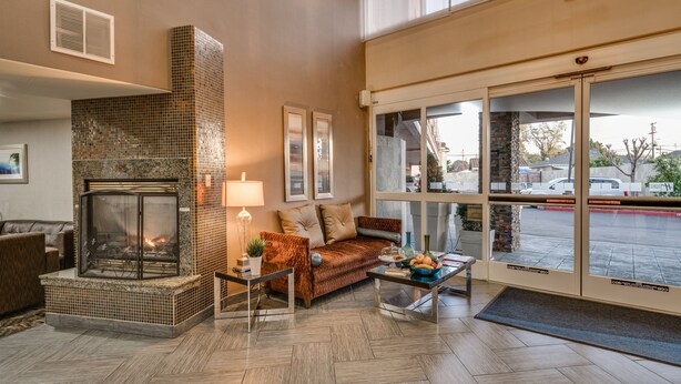 A lobby with a fireplace, seating area, and large windows overlooking a parking lot.