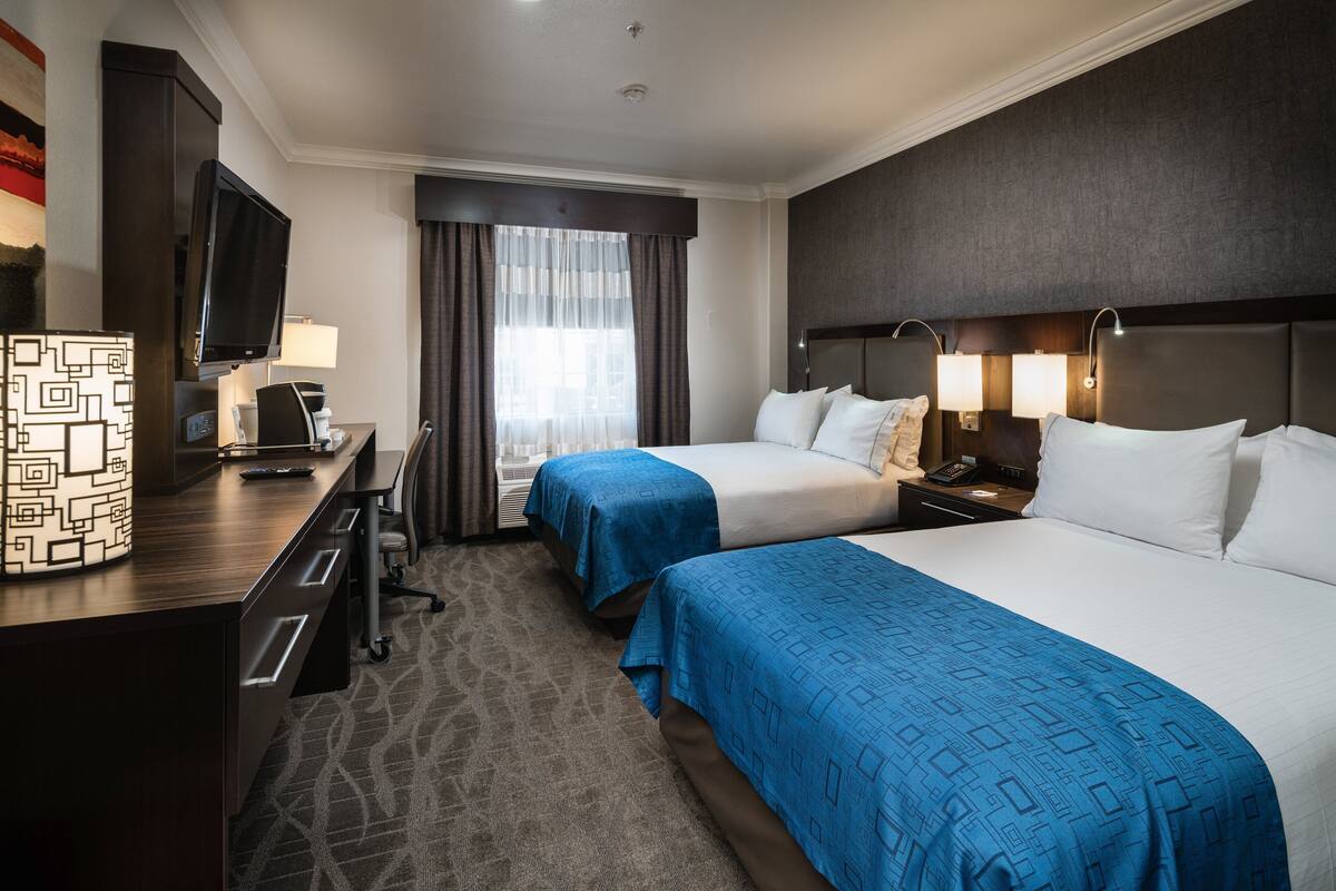 Une chambre d’hôtel avec deux lits, un bureau avec une télévision, une lampe et une table de chevet avec un téléphone.
